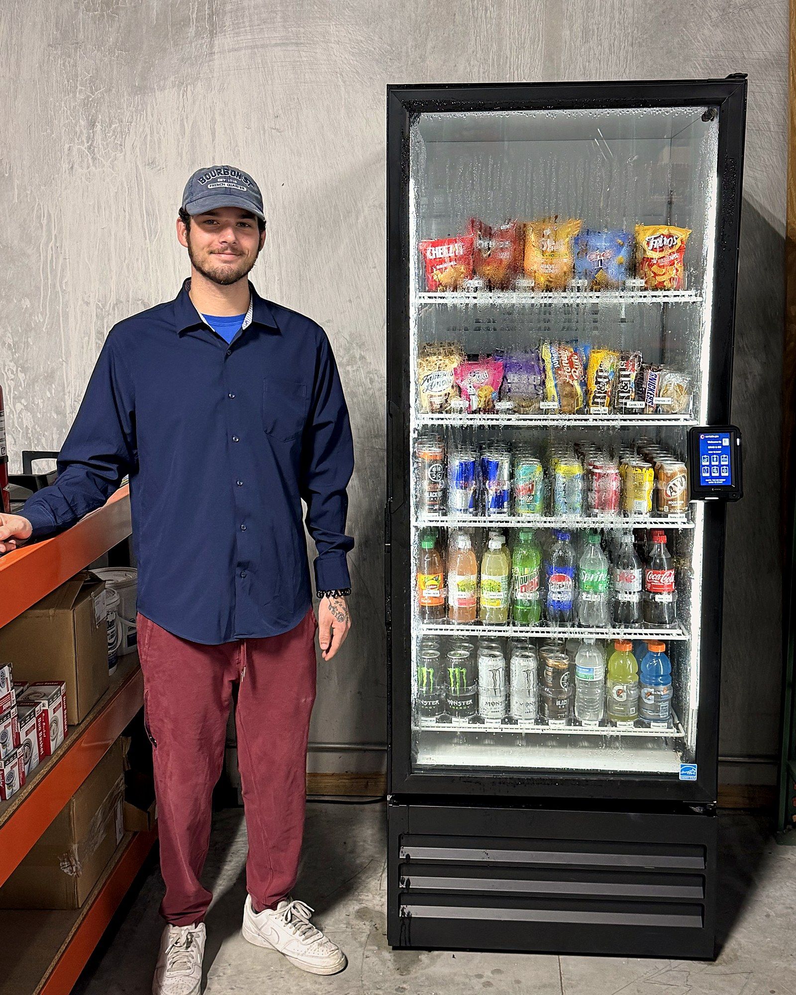 Craig Anthes standing beside a stocked glass-door vending machine.